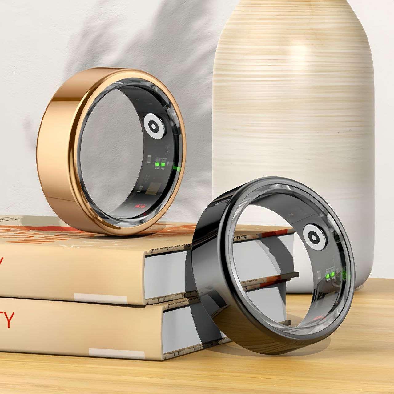 Two smart rings one in metallic rose gold and the other in glossy black with visible internal sensors, placed on stacked books beside a ceramic vase